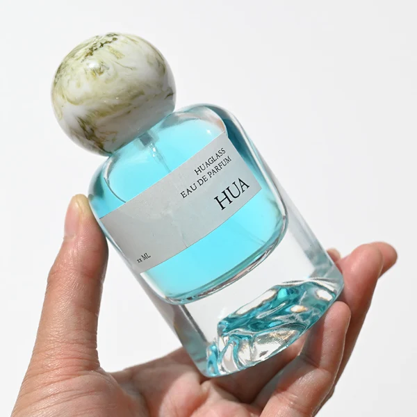 HUA0132 perfume bottle, cylindrical clear glass body with 30 ml, 50 ml, or 100 ml liquid, spherical plastic cap in milky white or black with marble texture, outer label with printed logo, modern minimalist design, ideal for gifting and daily use.