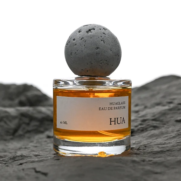HUA0134 perfume bottle, cylindrical clear glass body with 30 ml, 50 ml, or 100 ml liquid, spherical artificial stone cap, outer label with printed logo, modern minimalist design, ideal for gifting and daily use.