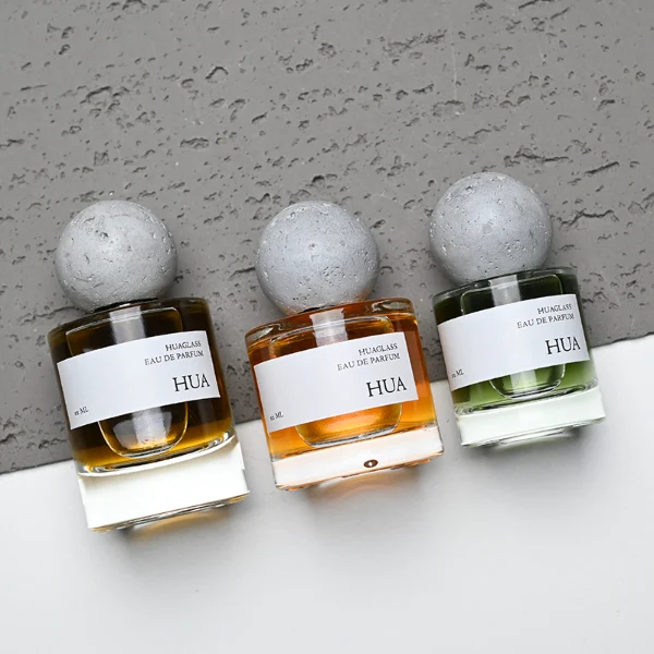 HUA0134 perfume bottle, cylindrical clear glass body with 30 ml, 50 ml, or 100 ml liquid, spherical artificial stone cap, outer label with printed logo, modern minimalist design, ideal for gifting and daily use.