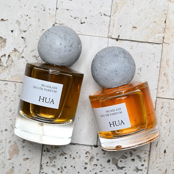 HUA0134 perfume bottle, cylindrical clear glass body with 30 ml, 50 ml, or 100 ml liquid, spherical artificial stone cap, outer label with printed logo, modern minimalist design, ideal for gifting and daily use.
