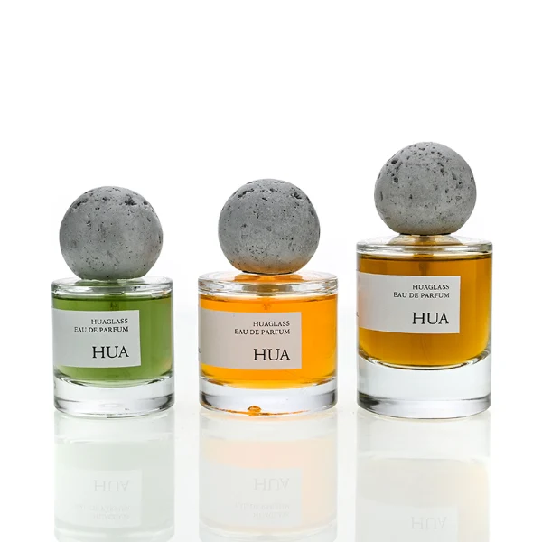 HUA0134 perfume bottle, cylindrical clear glass body with 30 ml, 50 ml, or 100 ml liquid, spherical artificial stone cap, outer label with printed logo, modern minimalist design, ideal for gifting and daily use.