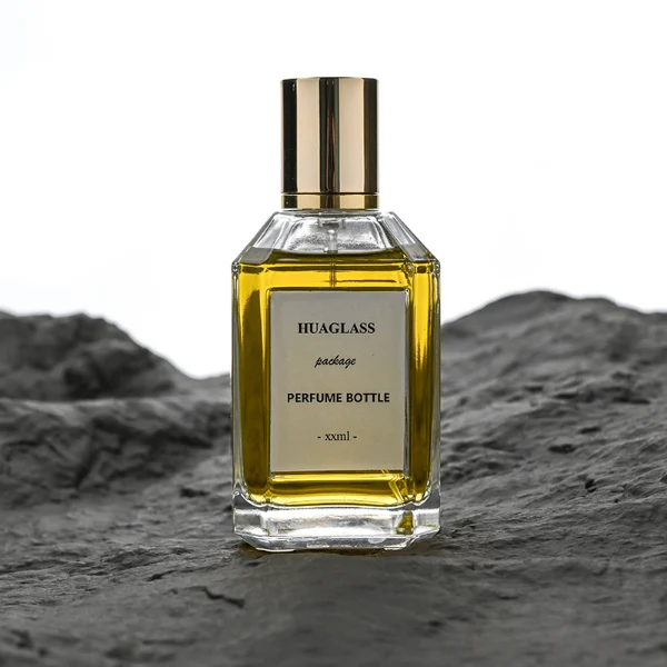 HUA0135 perfume bottle, rectangular clear glass body with 30 ml, 50 ml, or 100 ml liquid, cylindrical plastic cap with gold metallic neck, outer label with printed logo, modern elegant design, ideal for gifting and daily use.