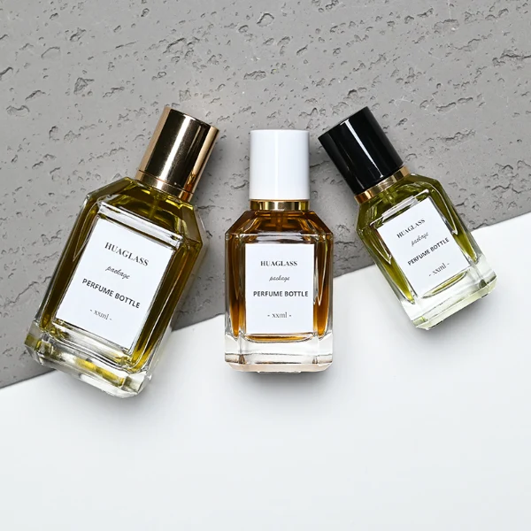 HUA0135 perfume bottle, rectangular clear glass body with 30 ml, 50 ml, or 100 ml liquid, cylindrical plastic cap with gold metallic neck, outer label with printed logo, modern elegant design, ideal for gifting and daily use.