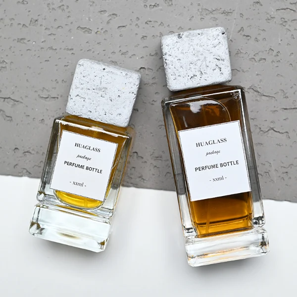 HUA0136 perfume bottle, rectangular clear glass body with 30 ml, 50 ml, or 100 ml liquid, square cement cap, outer label with printed logo, modern minimalist design, ideal for gifting and daily use.