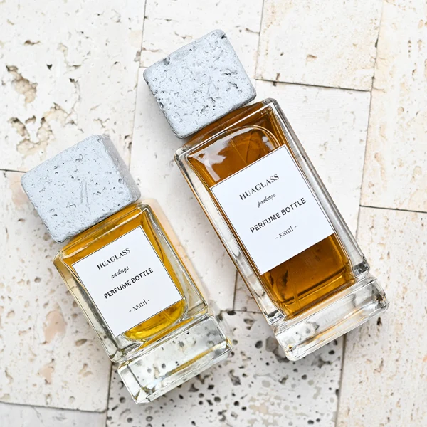 HUA0136 perfume bottle, rectangular clear glass body with 30 ml, 50 ml, or 100 ml liquid, square cement cap, outer label with printed logo, modern minimalist design, ideal for gifting and daily use.