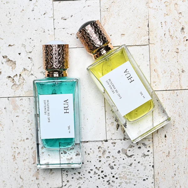 HUA0137 perfume bottle, square customizable glass body with 30 ml or 50 ml liquid, spherical plastic cap with gold metallic neck, outer label with printed logo, modern elegant design, ideal for gifting and daily use.