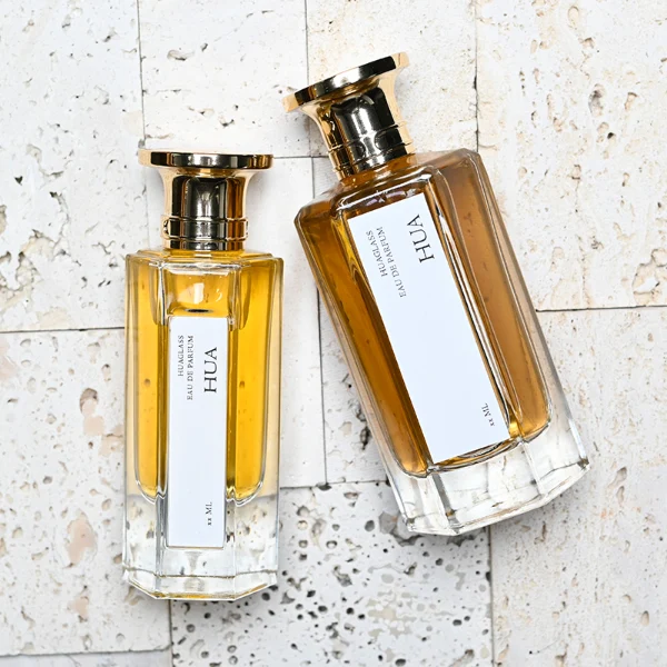 HUA0140 perfume bottle, hexagonal clear glass body with 50 ml or 100 ml liquid, Zamac cap with conical funnel top and cylindrical base with ring detailing, outer label with printed logo, modern elegant design, ideal for gifting and daily use.