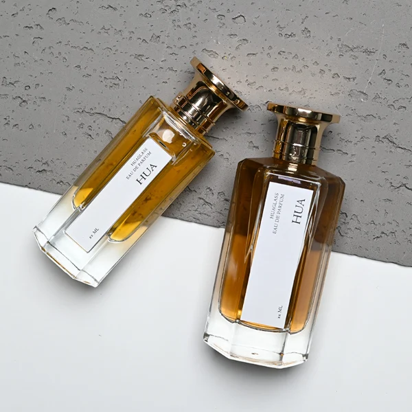 HUA0140 perfume bottle, hexagonal clear glass body with 50 ml or 100 ml liquid, Zamac cap with conical funnel top and cylindrical base with ring detailing, outer label with printed logo, modern elegant design, ideal for gifting and daily use.