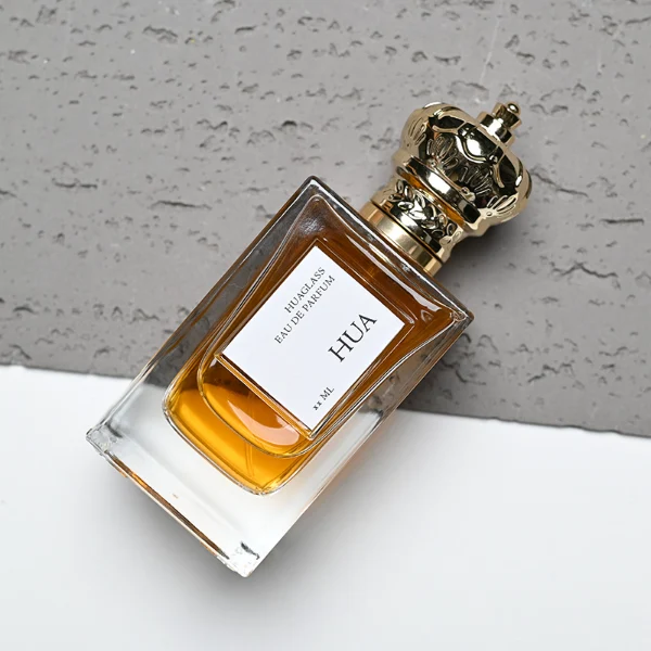 HUA0141 perfume bottle, rectangular clear glass body with 50 ml or 100 ml liquid, crown-shaped plastic cap with gold metallic neck, outer label with printed logo, modern luxurious design, ideal for gifting and daily use.