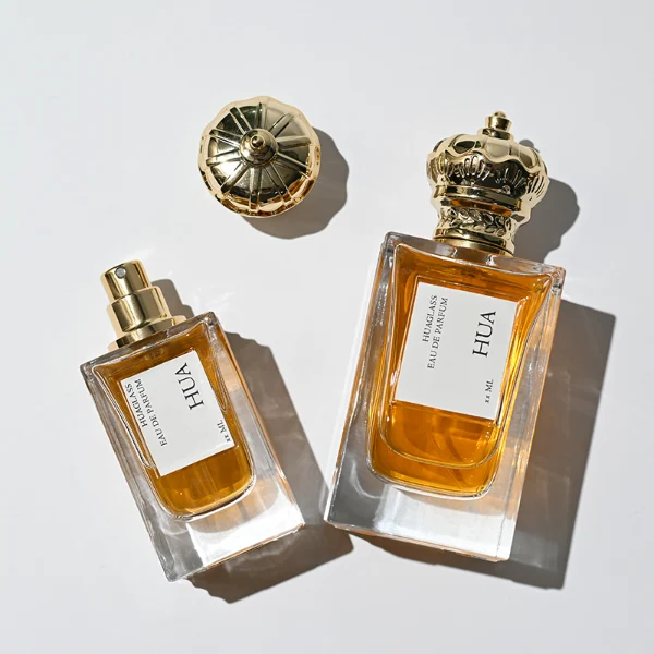 HUA0141 perfume bottle, rectangular clear glass body with 50 ml or 100 ml liquid, crown-shaped plastic cap with gold metallic neck, outer label with printed logo, modern luxurious design, ideal for gifting and daily use.