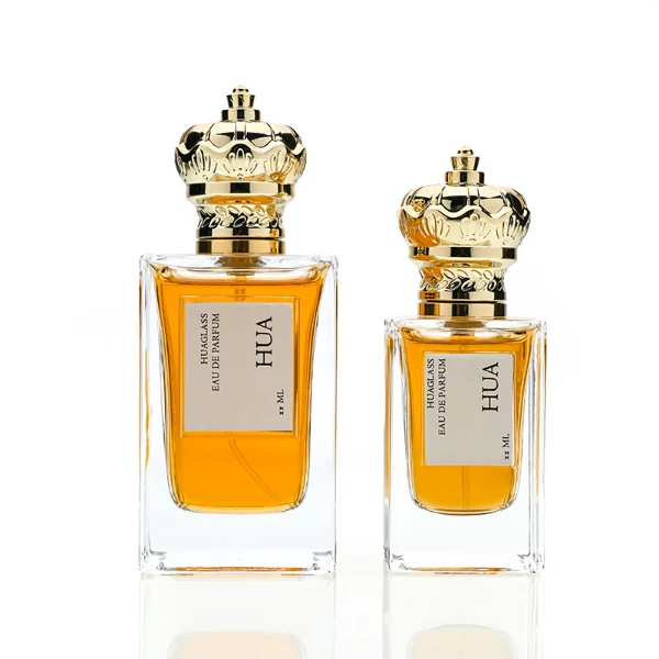 HUA0141 perfume bottle, rectangular clear glass body with 50 ml or 100 ml liquid, crown-shaped plastic cap with gold metallic neck, outer label with printed logo, modern luxurious design, ideal for gifting and daily use.