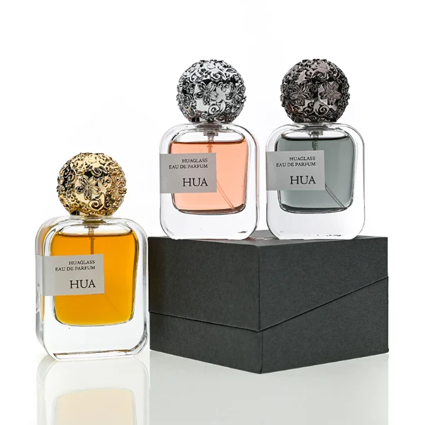 HUA0142 perfume bottle, square clear glass body with 30 ml, 50 ml, or 100 ml liquid, ornate spherical Zamac cap with embossed patterns, outer label with printed logo, modern luxurious design, ideal for gifting and daily use.