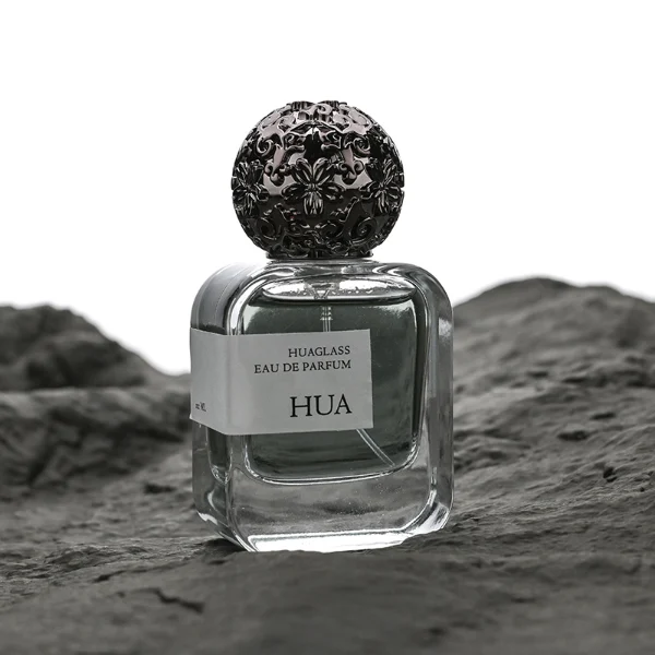 HUA0142 perfume bottle, square clear glass body with 30 ml, 50 ml, or 100 ml liquid, ornate spherical Zamac cap with embossed patterns, outer label with printed logo, modern luxurious design, ideal for gifting and daily use.
