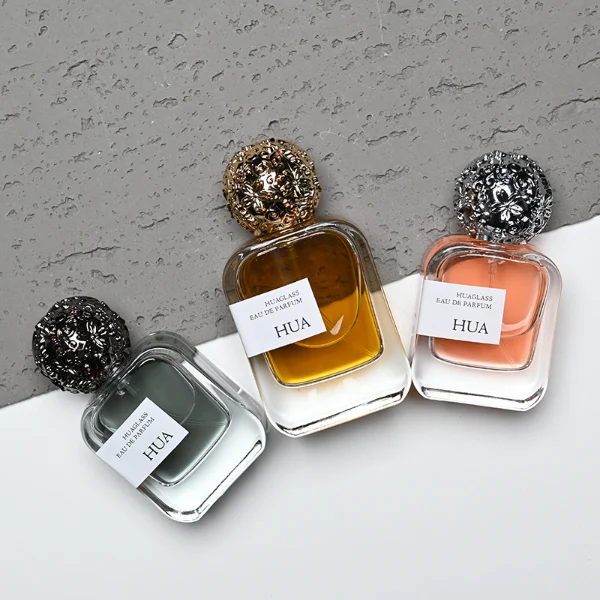 HUA0142 perfume bottle, square clear glass body with 30 ml, 50 ml, or 100 ml liquid, ornate spherical Zamac cap with embossed patterns, outer label with printed logo, modern luxurious design, ideal for gifting and daily use.