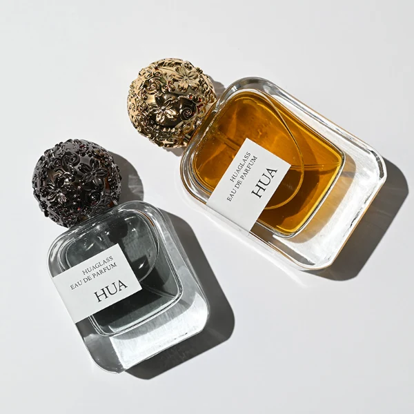 HUA0142 perfume bottle, square clear glass body with 30 ml, 50 ml, or 100 ml liquid, ornate spherical Zamac cap with embossed patterns, outer label with printed logo, modern luxurious design, ideal for gifting and daily use.