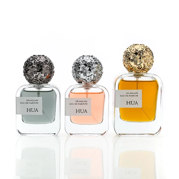 HUA0142 perfume bottle, square clear glass body with 30 ml, 50 ml, or 100 ml liquid, ornate spherical Zamac cap with embossed patterns, outer label with printed logo, modern luxurious design, ideal for gifting and daily use.