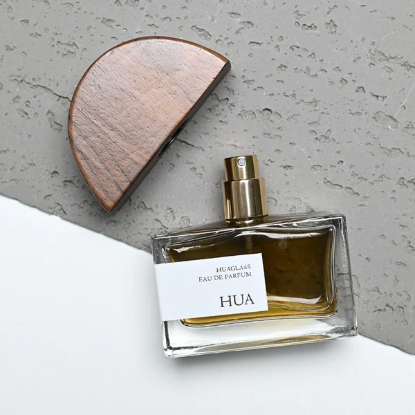 HUA0144 perfume bottle, rectangular clear glass body with 30 ml, 50 ml, or 100 ml liquid, half-circle wooden cap with gold metallic neck, outer label with printed logo, modern elegant design, ideal for gifting and daily use.