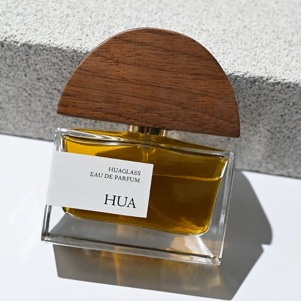 HUA0144 perfume bottle, rectangular clear glass body with 30 ml, 50 ml, or 100 ml liquid, half-circle wooden cap with gold metallic neck, outer label with printed logo, modern elegant design, ideal for gifting and daily use.