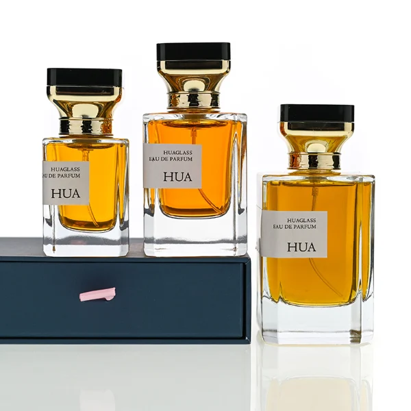 HUA0145 perfume bottle, rectangular clear glass body with 30 ml, 50 ml, or 100 ml liquid, gold funnel-shaped cap with black circular top inset with irregular transparent plastic piece, outer label with printed logo, modern luxurious design, ideal for gifting and daily use.