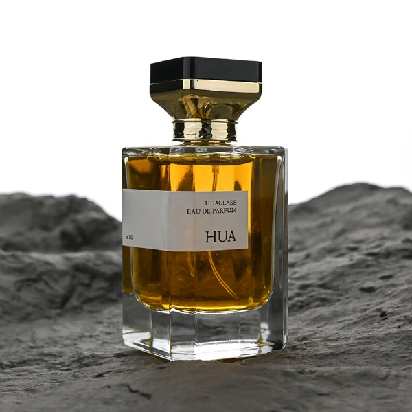 HUA0145 perfume bottle, rectangular clear glass body with 30 ml, 50 ml, or 100 ml liquid, gold funnel-shaped cap with black circular top inset with irregular transparent plastic piece, outer label with printed logo, modern luxurious design, ideal for gifting and daily use.