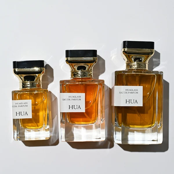 HUA0145 perfume bottle, rectangular clear glass body with 30 ml, 50 ml, or 100 ml liquid, gold funnel-shaped cap with black circular top inset with irregular transparent plastic piece, outer label with printed logo, modern luxurious design, ideal for gifting and daily use.