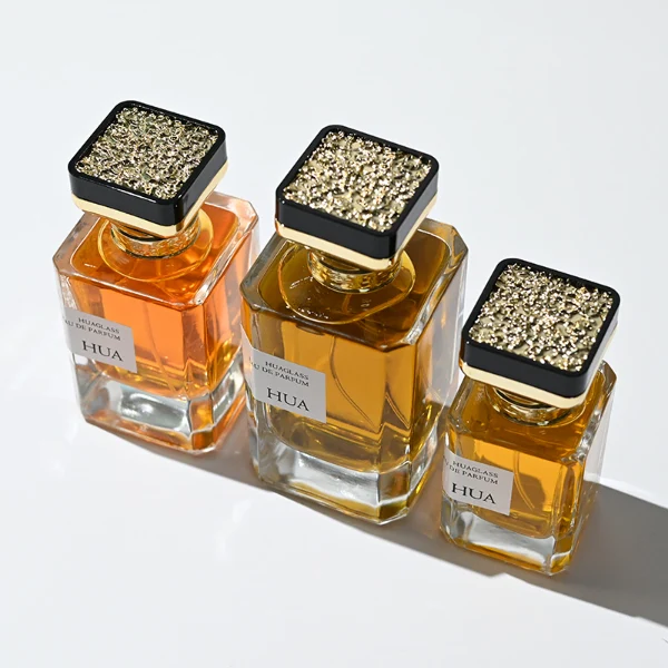 HUA0145 perfume bottle, rectangular clear glass body with 30 ml, 50 ml, or 100 ml liquid, gold funnel-shaped cap with black circular top inset with irregular transparent plastic piece, outer label with printed logo, modern luxurious design, ideal for gifting and daily use.