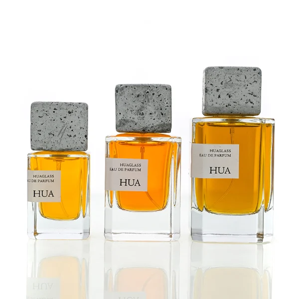HUA0153 perfume bottle, rectangular clear glass body with 30 ml, 50 ml, or 100 ml liquid, square cement cap, outer label with printed logo, modern elegant design, ideal for gifting and daily use.
