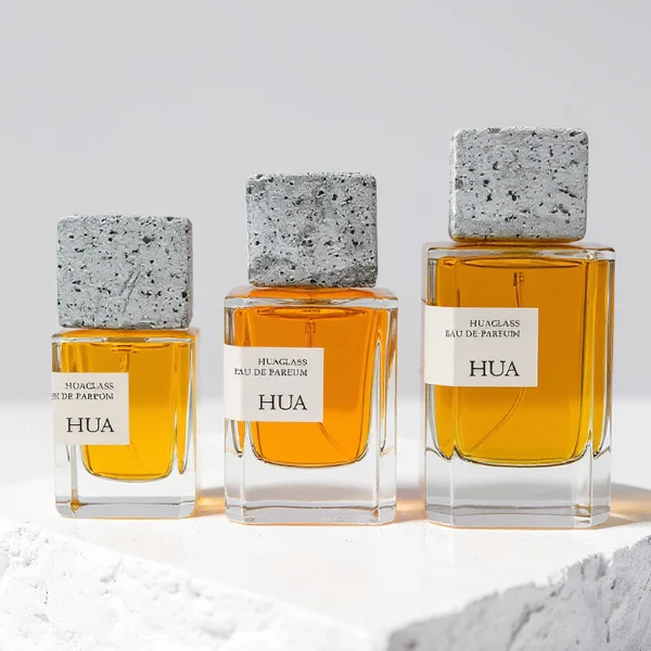 HUA0153 perfume bottle, rectangular clear glass body with 30 ml, 50 ml, or 100 ml liquid, square cement cap, outer label with printed logo, modern elegant design, ideal for gifting and daily use.