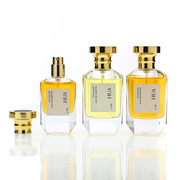 HUA0156 perfume bottle, multifaceted clear glass body with 30 ml, 50 ml, or 100 ml liquid, cylindrical cap with flat top and stepped base in gold, outer label with printed logo, modern elegant design, ideal for gifting and daily use.