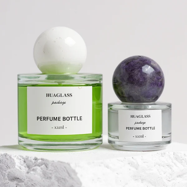 HUA0157 perfume bottle, cylindrical clear glass body with 30 ml, 50 ml, or 100 ml liquid, spherical crystal stone cap, outer label with printed logo, modern elegant design, ideal for gifting and daily use.