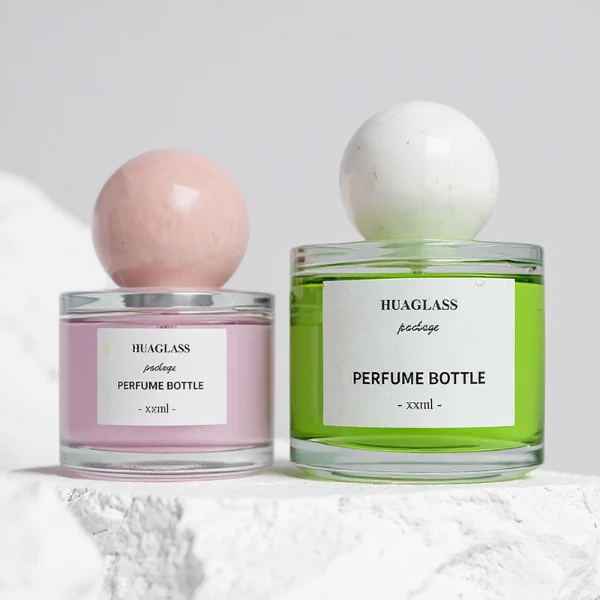 HUA0157 perfume bottle, cylindrical clear glass body with 30 ml, 50 ml, or 100 ml liquid, spherical crystal stone cap, outer label with printed logo, modern elegant design, ideal for gifting and daily use.