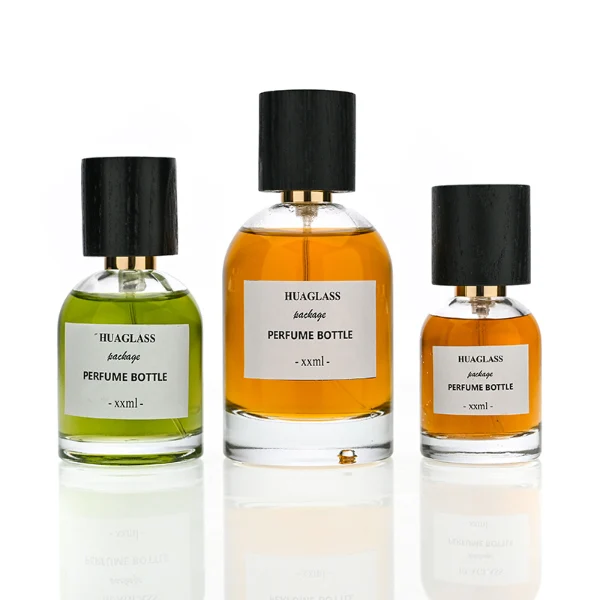 HUA0162 perfume bottle, cylindrical transparent glass body with 30 ml, 50 ml, or 100 ml liquid, tall cylindrical black wooden cap with gold metallic neck, outer label with printed logo, modern elegant design, ideal for gifting and daily use.
