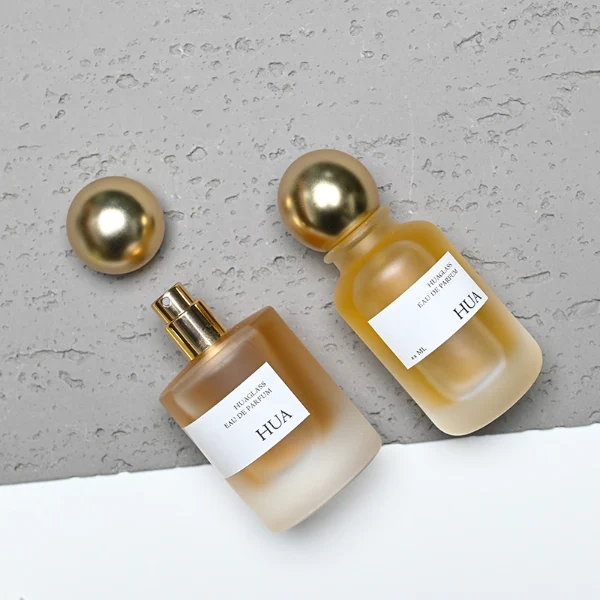 HUA0164 perfume bottle, cylindrical frosted glass body with 30 ml, 50 ml, or 100 ml liquid, spherical gold-colored plastic cap, outer label with printed logo, modern elegant design, ideal for gifting and daily use.
