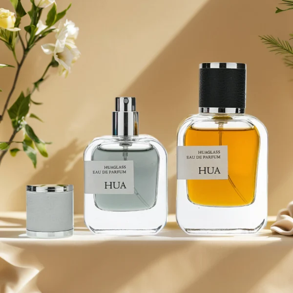 HUA0165 perfume bottle, rectangular transparent glass body with 30 ml, 50 ml, or 100 ml liquid, cylindrical plastic cap wrapped in leather with gold metallic neck, outer label with printed logo, modern elegant design, ideal for gifting and daily use.