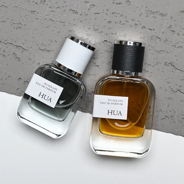 HUA0165 perfume bottle, rectangular transparent glass body with 30 ml, 50 ml, or 100 ml liquid, cylindrical plastic cap wrapped in leather with gold metallic neck, outer label with printed logo, modern elegant design, ideal for gifting and daily use.