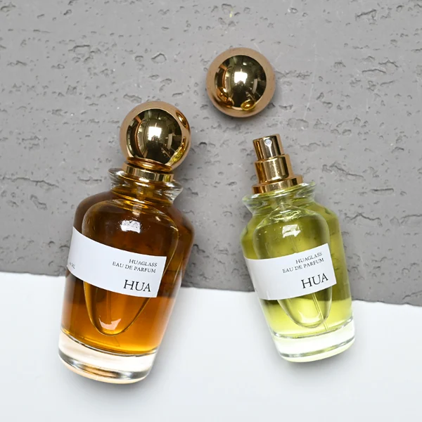 HUA0167 perfume bottle, kettle-shaped cylindrical transparent glass body with 50 ml or 100 ml liquid, spherical glossy plastic cap with gold neck, outer label with printed logo, modern elegant design, ideal for gifting and daily use.