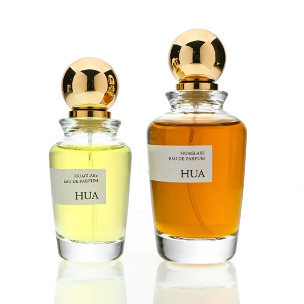 HUA0167 perfume bottle, kettle-shaped cylindrical transparent glass body with 50 ml or 100 ml liquid, spherical glossy plastic cap with gold neck, outer label with printed logo, modern elegant design, ideal for gifting and daily use.