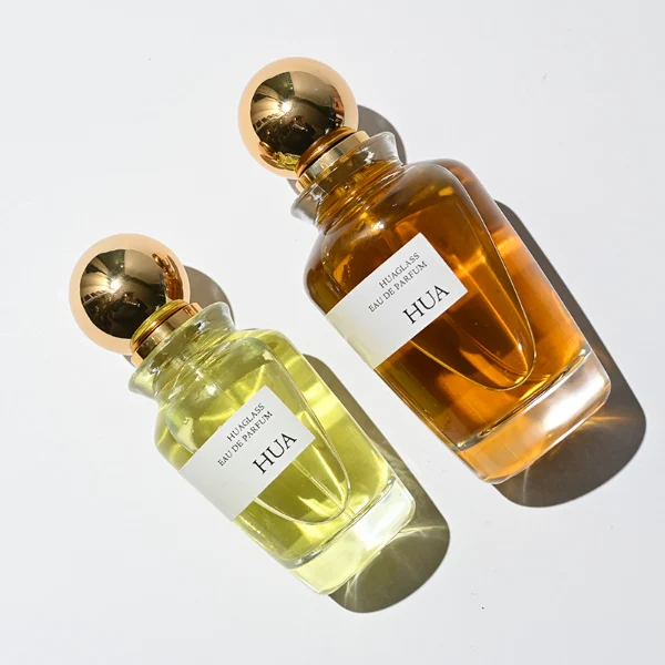 HUA0167 perfume bottle, kettle-shaped cylindrical transparent glass body with 50 ml or 100 ml liquid, spherical glossy plastic cap with gold neck, outer label with printed logo, modern elegant design, ideal for gifting and daily use.