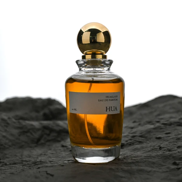 HUA0167 perfume bottle, kettle-shaped cylindrical transparent glass body with 50 ml or 100 ml liquid, spherical glossy plastic cap with gold neck, outer label with printed logo, modern elegant design, ideal for gifting and daily use.