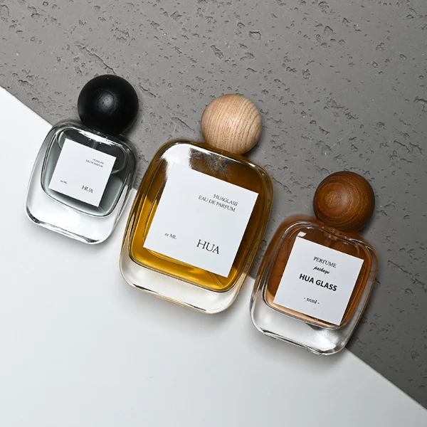 HUA0168 perfume bottle, rectangular transparent glass body with 30 ml, 50 ml, or 100 ml liquid, spherical wooden cap, outer label with printed logo, modern natural elegant design, ideal for gifting and daily use.