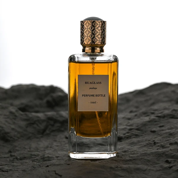HUA0170 perfume bottle, rectangular transparent glass body with 50 ml or 80 ml liquid, cylindrical plastic cap with engraved decorative pattern and gold neck ring, outer label with printed logo, modern luxurious design, ideal for gifting and daily use.