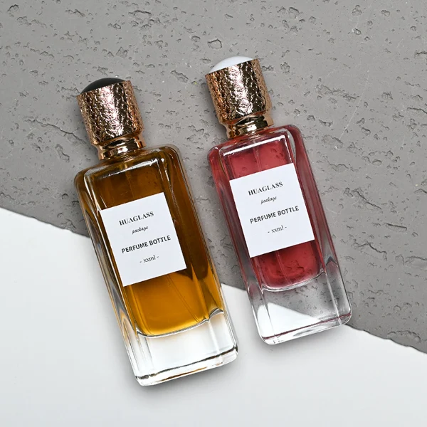 HUA0170 perfume bottle, rectangular transparent glass body with 50 ml or 80 ml liquid, cylindrical plastic cap with engraved decorative pattern and gold neck ring, outer label with printed logo, modern luxurious design, ideal for gifting and daily use.