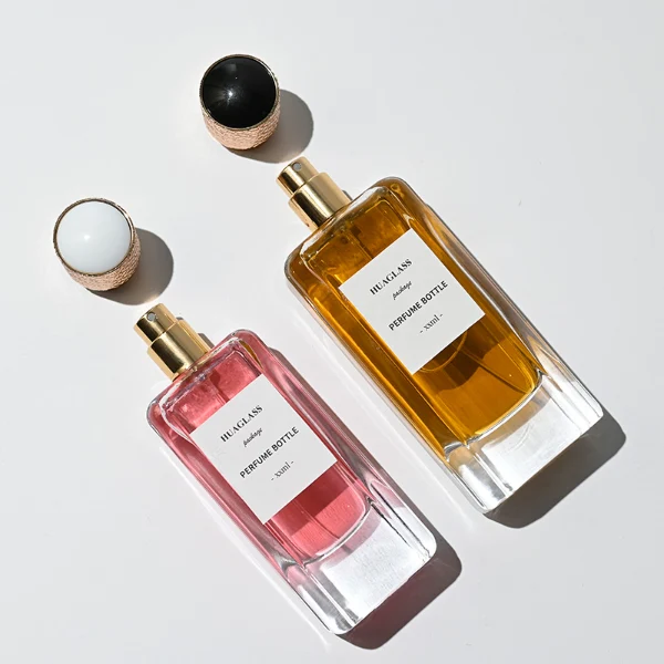 HUA0170 perfume bottle, rectangular transparent glass body with 50 ml or 80 ml liquid, cylindrical plastic cap with engraved decorative pattern and gold neck ring, outer label with printed logo, modern luxurious design, ideal for gifting and daily use.
