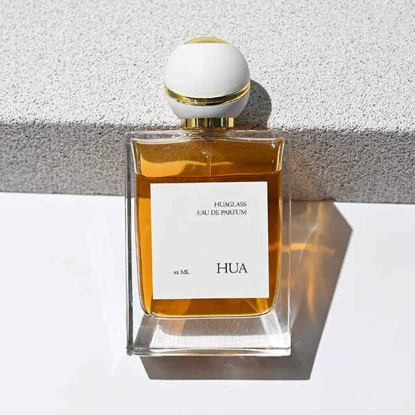 HUA0171 perfume bottle, rectangular transparent glass body with 30 ml, 50 ml, or 100 ml liquid, spherical plastic cap with diagonal gold stripe detailing and gold neck ring, outer label with printed logo, modern elegant design, ideal for gifting and daily use.