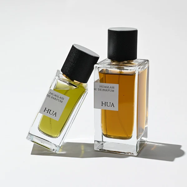 HUA0172 perfume bottle, rectangular transparent glass body with 30 ml, 50 ml, or 100 ml liquid, smooth black cylindrical plastic cap with gold sprayer and gold neck ring, outer label with printed logo, modern minimalist design, ideal for gifting and daily use.