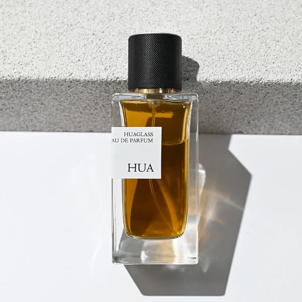 HUA0172 perfume bottle, rectangular transparent glass body with 30 ml, 50 ml, or 100 ml liquid, smooth black cylindrical plastic cap with gold sprayer and gold neck ring, outer label with printed logo, modern minimalist design, ideal for gifting and daily use.