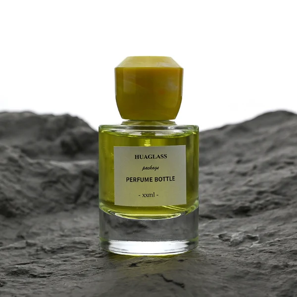HUA0174 perfume bottle, cylindrical transparent glass body with 30 ml, 50 ml, or 100 ml liquid, faceted geometric plastic cap with marble-effect appearance, printed logo label, modern artistic luxury design, ideal for gifting and daily use.