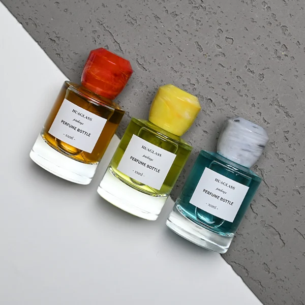 HUA0174 perfume bottle, cylindrical transparent glass body with 30 ml, 50 ml, or 100 ml liquid, faceted geometric plastic cap with marble-effect appearance, printed logo label, modern artistic luxury design, ideal for gifting and daily use.