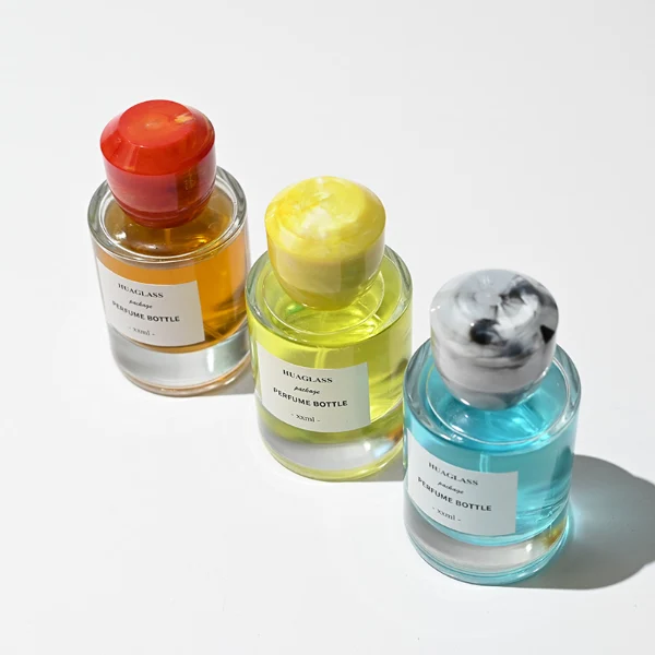 HUA0174 perfume bottle, cylindrical transparent glass body with 30 ml, 50 ml, or 100 ml liquid, faceted geometric plastic cap with marble-effect appearance, printed logo label, modern artistic luxury design, ideal for gifting and daily use.
