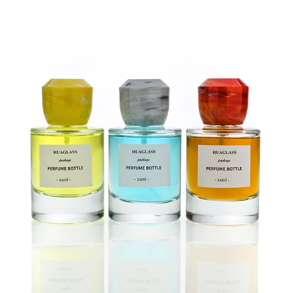 HUA0174 perfume bottle, cylindrical transparent glass body with 30 ml, 50 ml, or 100 ml liquid, faceted geometric plastic cap with marble-effect appearance, printed logo label, modern artistic luxury design, ideal for gifting and daily use.